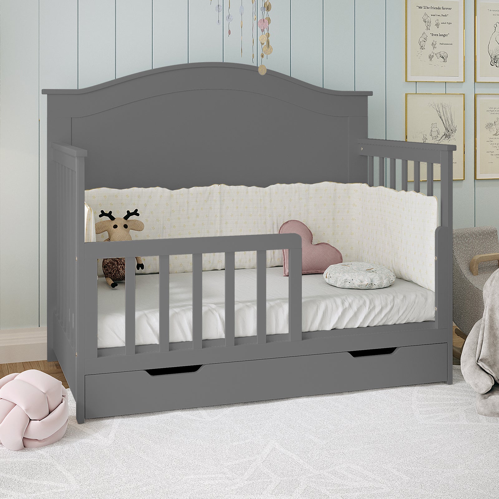 Giro Solid Pine Toddler Bed Rail Kit Grey displayed as a small convertible toddler bed with safety rails, a pull-out drawer, plush deer toy, pink heart pillow, and a soft cushion in a nursery setting.