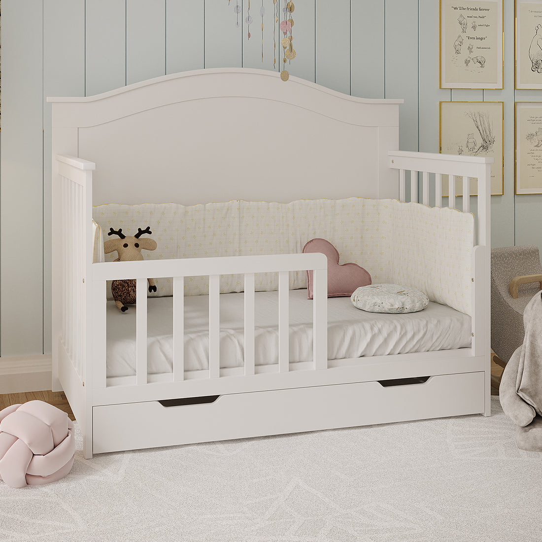 Giro Solid Pine Toddler Bed Rail Kit - White shown installed on a white wooden crib with soft bumpers, plush toys, and a pull-out drawer, creating a cozy nursery corner.