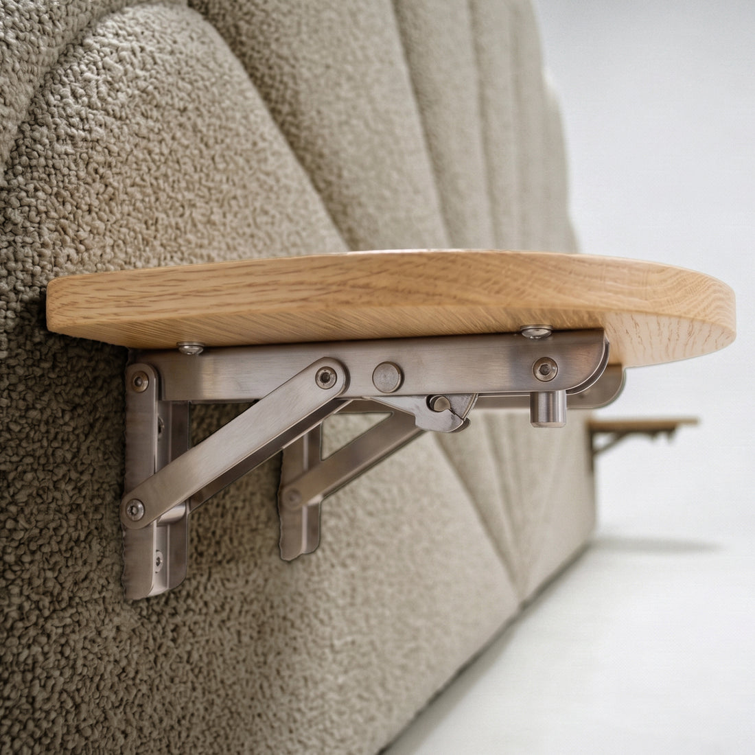 Close-up of a fold-down wooden shelf attached to a beige boucle upholstered headboard, showing the brushed metal bracket