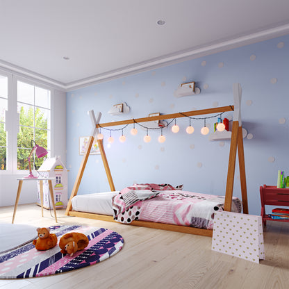 Helena Kids Single Solid Pine Teepee Bed Frame in Natural, featuring a teepee-style design with pink, white, and black bedding, adorned with glowing fairy lights, set against a playful, polka-dotted wall.