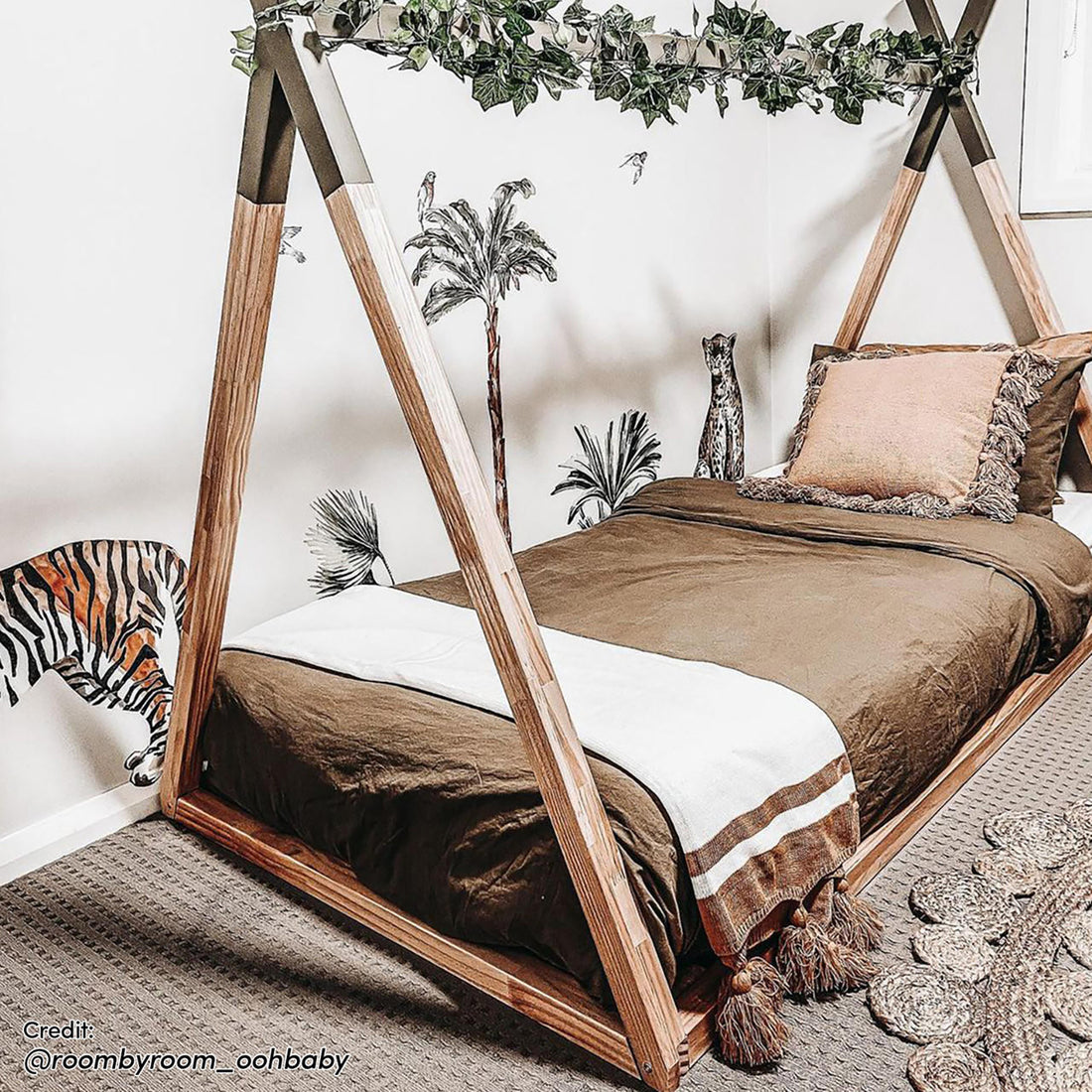 Helena Kids Single Solid Pine Teepee Bed Frame in Natural, styled with earthy bedding and a faux-ivy garland, set against a jungle-themed wall, creating a playful and cozy children's bedroom corner.