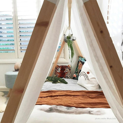 Helena Kids Single Solid Pine Teepee Bed Frame in Natural, showcasing a light wood A-frame and off-white canvas, accented with whimsical cushions, a plush toy, and a hanging planter for a playful retreat.
