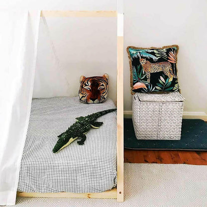 Helena Kids Single Solid Pine Teepee Bed Frame in Natural with a black-and-white grid sheet, a crocodile plush toy, tiger head cushion, and adjacent white basket with a jungle-themed pillow.