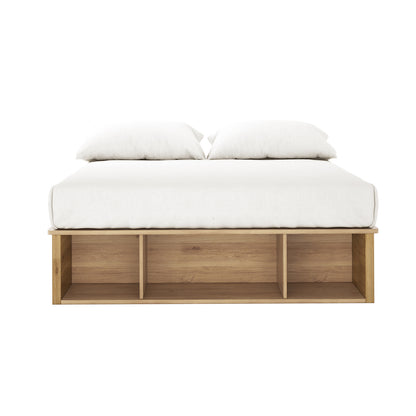 Herais Double Platform Bed Base with Storage in Oak, featuring a white mattress and pillows on a low wooden frame with three open storage compartments at the foot end.