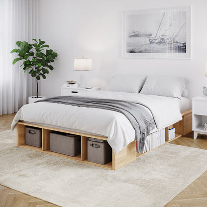 Herais Queen Platform Bed Base with Storage in Oak features a light-wood low platform, integrated storage cubbies holding baskets and books, and a clean, minimalist design with white bedding and a gray throw.