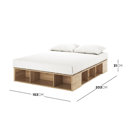 Herais Queen Platform Bed Base with Storage in Oak, showcasing a low-profile wooden frame with integrated open cubbies, mattress, and pillows. Features ten side compartments and two footboard cubbies.