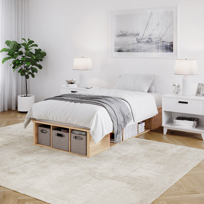 Herais Single Platform Bed Base with Storage in Oak features a low wooden frame, white linens, built-in shelving with fabric bins, and minimalist design, complemented by matching nightstands and a nautical-themed print.