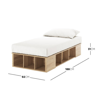 Herais Single Platform Bed Base with Storage in Oak, featuring a low-profile frame with open cubbyhole storage on sides and foot, topped with a thin mattress and pillow, ideal for organized living.