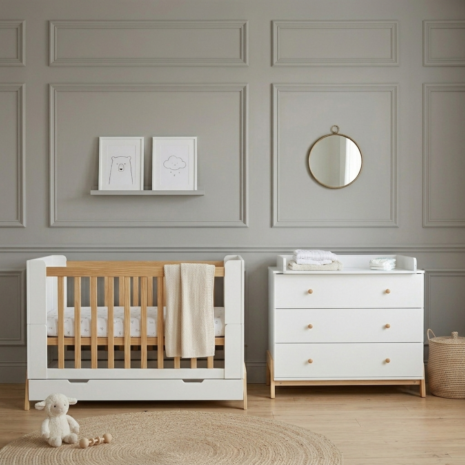 White and natural wood baby cot with storage drawer beside white chest of drawers in grey paneled nursery
