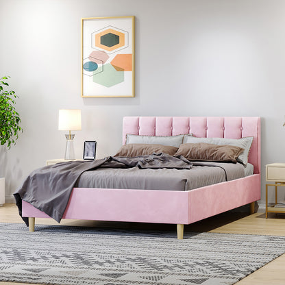 The Kelly Double Velvet Fabric Bed Frame in Pink features a blush-pink tufted headboard, dressed in grey linens, set in a modern bedroom with a light-wood nightstand and abstract art above.