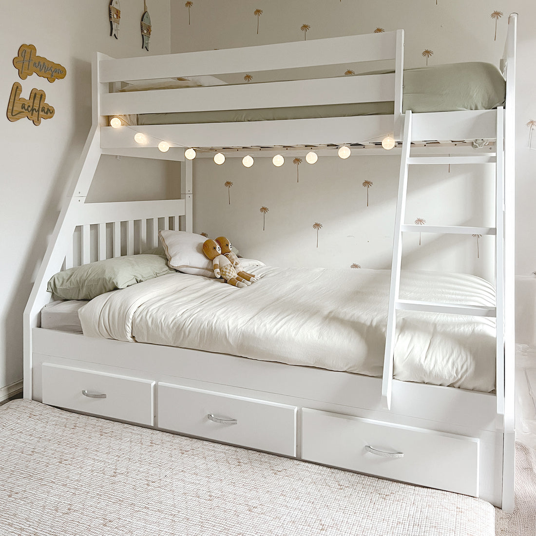 Kourtney Hardwood Triple Bunk Bed with Drawers in White, featuring a full lower bed, twin upper bed with safety rails, angled ladder, globe lights, and built-in storage drawers, surrounded by decorative wall decals.