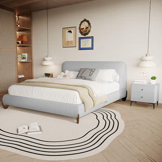 Laryn Queen Plush Bouclé Cloud Bed Frame in Light Grey, featuring a low-profile design with a padded headboard, dressed in white linens and a beige throw, creating a serene bedroom centerpiece.