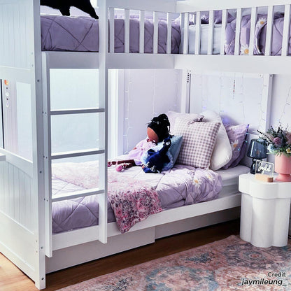 Lucy Solid Pine Wood Corner Triple Loft Bunk Bed in White, featuring a bunk with lavender bedding and a playful decor, surrounded by fairy lights, a side table with a lamp, and plush toys.