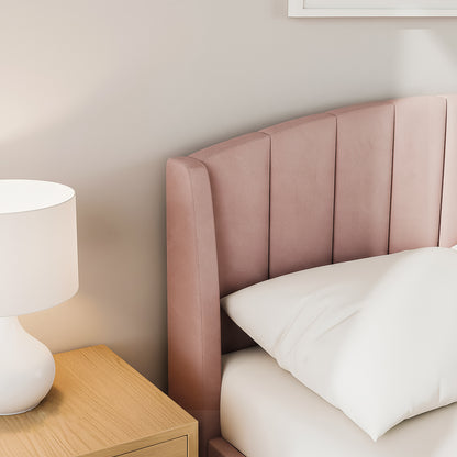 Lyra Queen Winged Velvet Fabric Bed Frame in Soft Pink featuring a channel-stitched headboard. Positioned next to a wooden nightstand with a white ceramic lamp, showcasing cozy bedroom elegance.