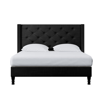 Maggie Double Winged Fabric Bed Frame – Black, featuring a deep-buttoned Chesterfield headboard. The black bed frame is complemented by white pillows and a white cushion on a black surface.