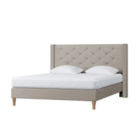 Maggie Queen Winged Fabric Bed Frame in Warm Grey features a tall, button-tufted headboard, low-profile frame, turned wooden legs, white mattress cover, and pillows, embodying elegance and stability.