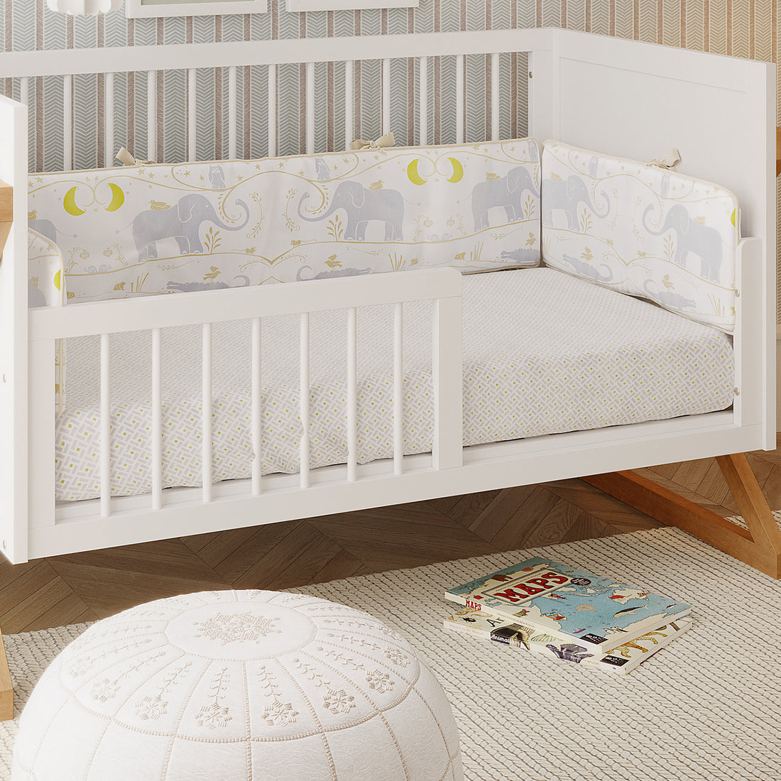 Melai Solid Pine 3-in-1 Cot to Toddler Bed Rail Kit in White, shown as a toddler bed with gray elephant-patterned bedding, enhancing a cozy nursery setting with books and a pouf on a woven rug.