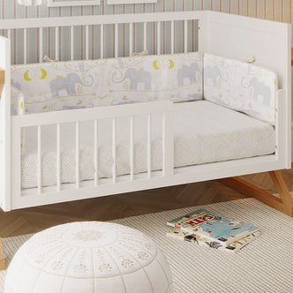 Melai Solid Pine 3-in-1 Cot to Toddler Bed Rail Kit in White, shown as a toddler bed with gray elephant-patterned bedding, enhancing a cozy nursery setting with books and a pouf on a woven rug.