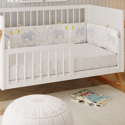 Melai Solid Pine 3-in-1 Cot to Toddler Bed Rail Kit in White, shown as a toddler bed with gray elephant-patterned bedding, enhancing a cozy nursery setting with books and a pouf on a woven rug.