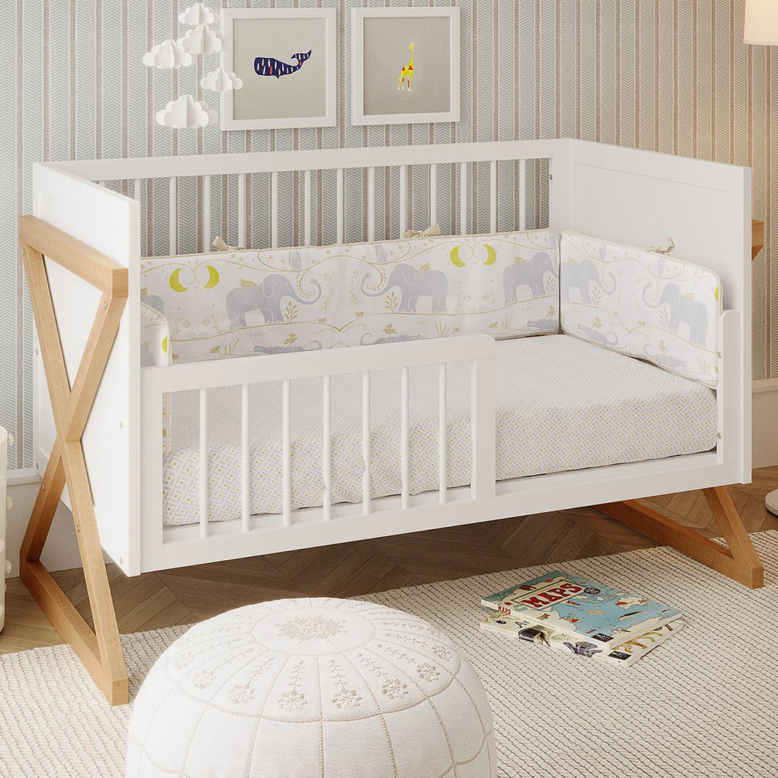 Melai Solid Pine Toddler Bed Rail Kit in white, installed on a crib with natural-wood “X” legs, surrounded by nursery decor including elephant-patterned bedding, a cloud mobile, and animal prints.