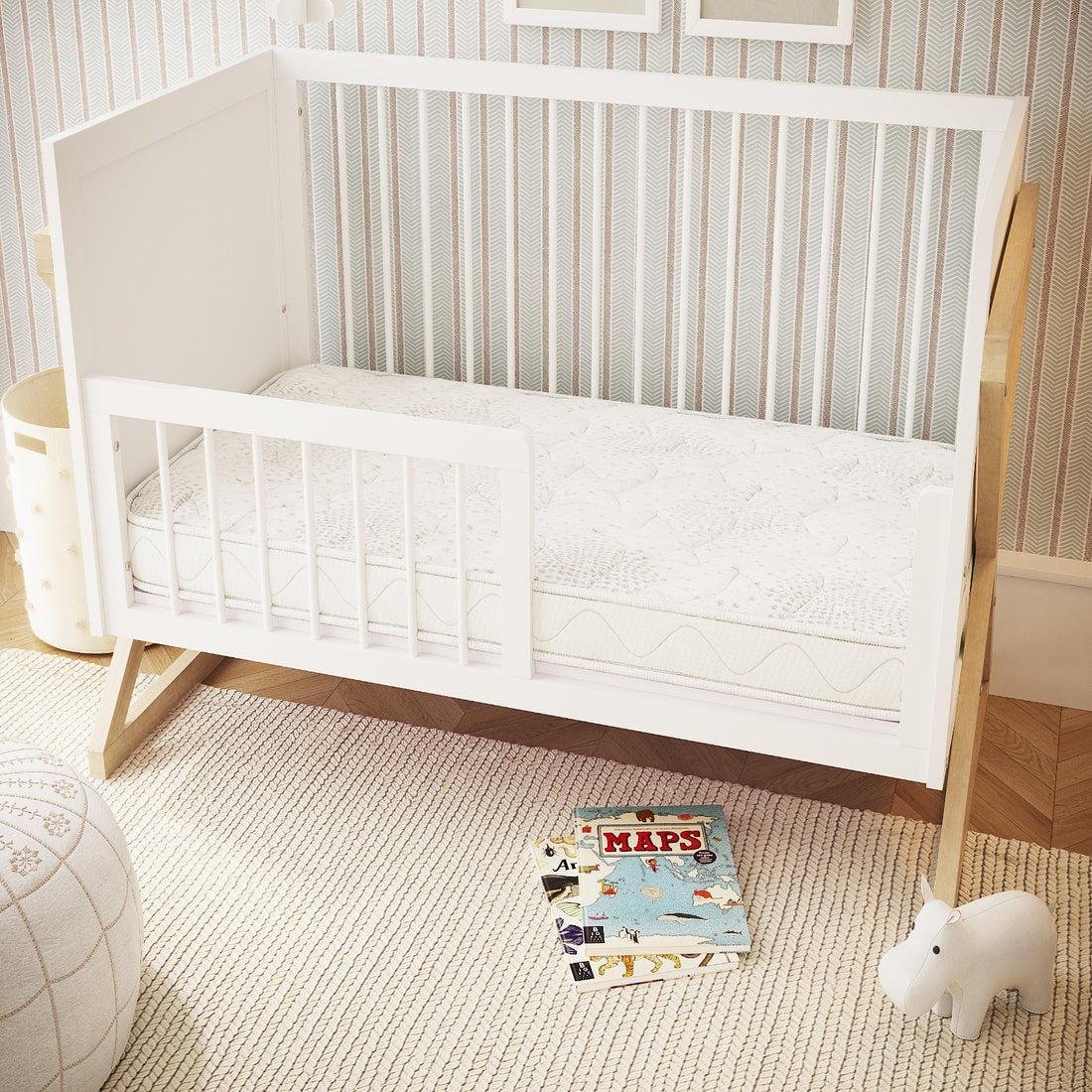 Gydas 10cm Knitted Cot Mattress with High-Density Foam in a white wooden toddler bed, surrounded by a woven rug, picture books, hippo toy, and storage basket in a serene nursery setting.