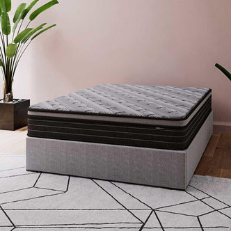 Phoebe Queen 33cm Euro Pillow Top Pocket Spring Mattress shown on a low gray bed base; features a dark gray top and black midsection, complemented by a geometric-patterned rug and greenery for a modern bedroom look.