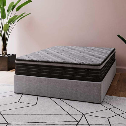 Phoebe Queen 33cm Euro Pillow Top Pocket Spring Mattress shown on a low gray bed base; features a dark gray top and black midsection, complemented by a geometric-patterned rug and greenery for a modern bedroom look.