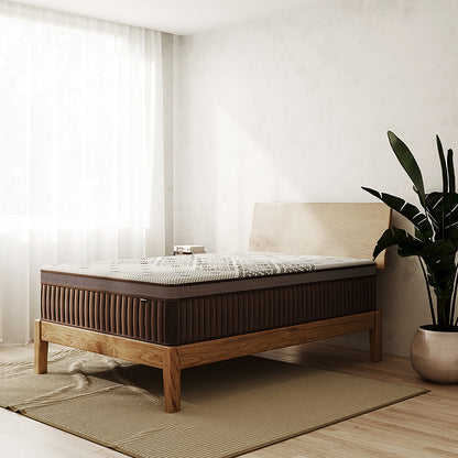 Thalia Double 30cm Memory Foam Pocket Spring Mattress in Med displayed in a minimalist bedroom, featuring a brown, textured surface on a wooden frame, set on a ribbed rug, with books on the headboard.