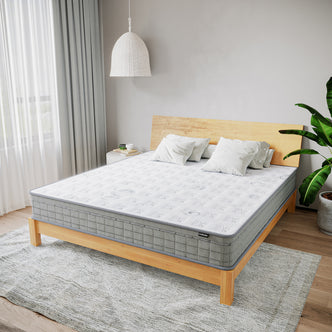 Thetis King 25cm Pocket Spring Latex Mattress in Med Firm on a wooden-frame bed, topped with white pillows, surrounded by a minimalist bedroom with a side table, potted plant, and sheer-curtained window.