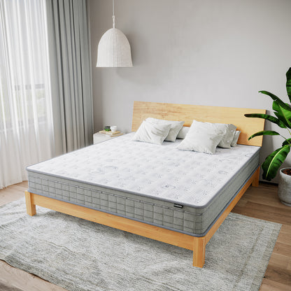 Thetis King 25cm Pocket Spring Latex Mattress in Med Firm on a wooden-frame bed, topped with white pillows, surrounded by a minimalist bedroom with a side table, potted plant, and sheer-curtained window.