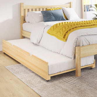 Narell Single Solid Wood Pull-Out Trundle Bed in Natural, featuring a light-wood frame with white bedding, a mustard quilt, and a matching trundle, set on a pale wood floor with a patterned rug.