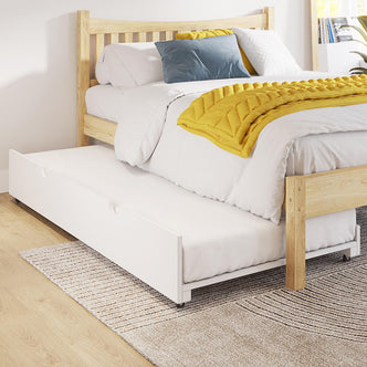 Narell Single Solid Wood Pull-Out Trundle Bed in White with a light-wood frame, white sheets, mustard-yellow throw, slate-blue cushion, and visible white trundle on caster wheels beneath.