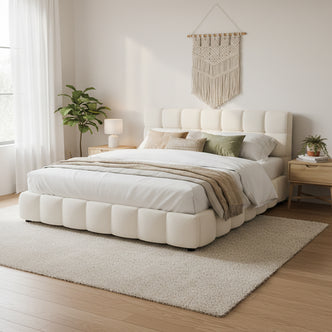 Nikias King Boucle Fabric Bed Frame in Cream White, featuring a tufted headboard and plush upholstery, set in a serene bedroom with matching nightstands, a macramé wall tapestry, and a leafy plant.