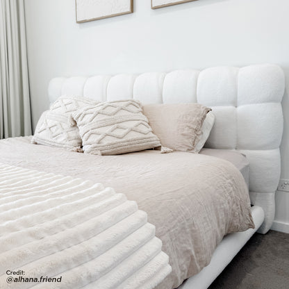 Nikias Super King Boucle Fabric Bed Frame in Cream White features a grid-tufted headboard, neutral-toned bedding, textured pillows, and a ribbed throw, creating a luxurious, monochromatic bedroom scene.