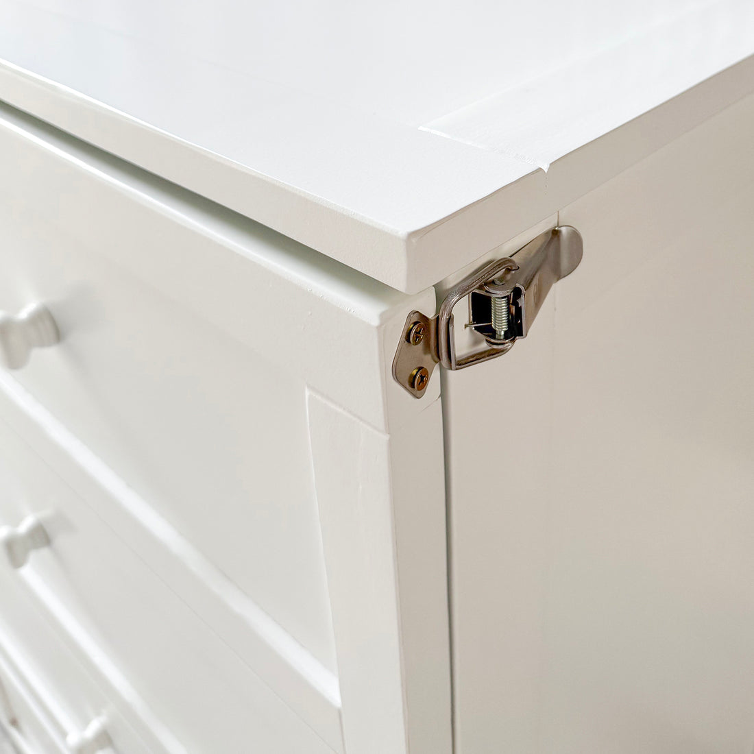 Close-up of the metal safety latch on the top corner of the white Murphy bed cabinet, ensuring secure closure