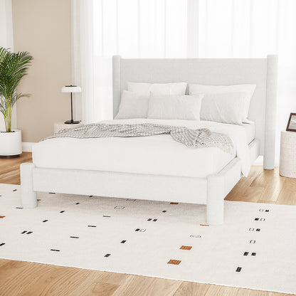 Rhoda Double Boucle Fabric Bed Frame in Cream White, featuring an oversized curved headboard and low-profile design, surrounded by white bedding, a gray throw, and minimalist side tables with decor.