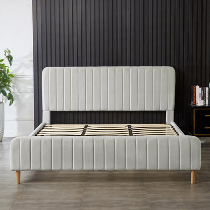 Seneca King Upholstered Velvet Bed – Slate in a minimalist bedroom, featuring a light-gray, vertically-channeled headboard and footboard on wooden legs, accompanied by a bedside cabinet and a potted plant.