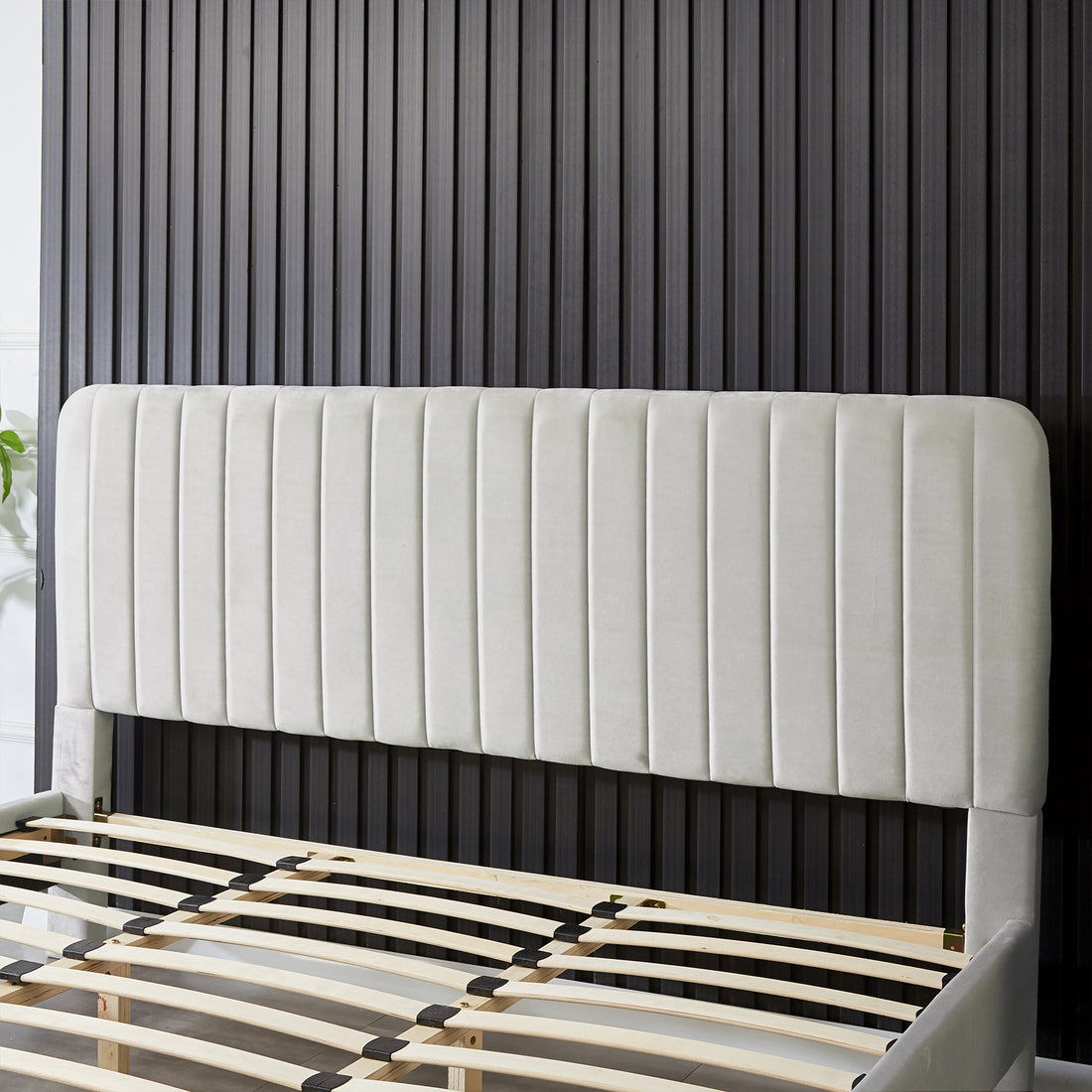 Seneca King Upholstered Velvet Bed – Slate, featuring a tall, padded headboard with vertical channel-tufting and a slatted wooden base, set against a dark ribbed wall panel.