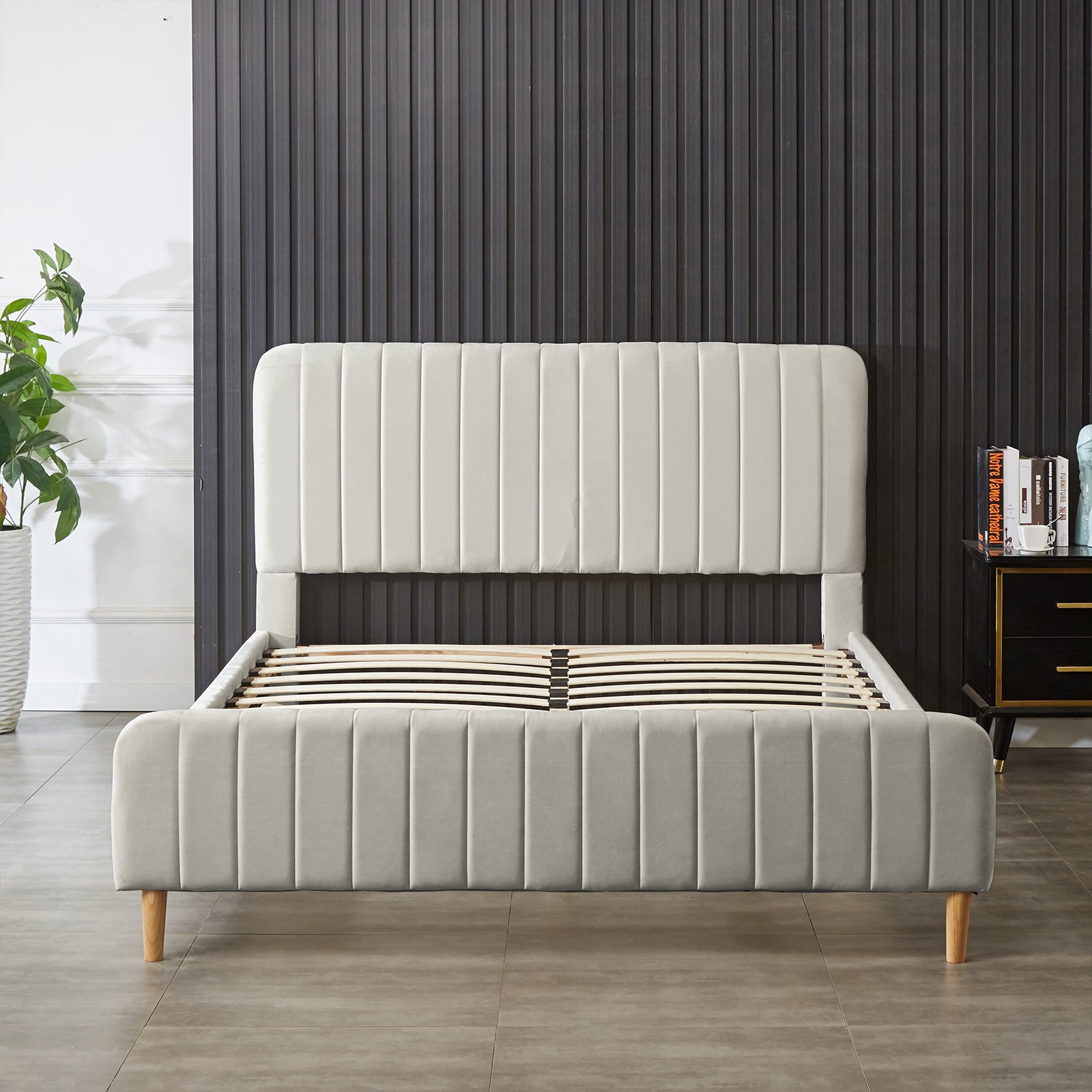 Seneca Queen Upholstered Velvet Bed – Slate: Modern platform bed with a tall, channeled headboard, light gray fabric, and wooden legs, featuring exposed slatted supports, adjacent to plant and bedside table.