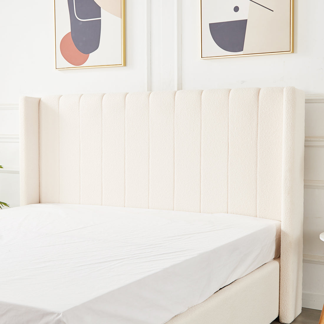 Septima & Fulvia Bouclé King Bed Base & Winged Headboard in Cream White, featuring a tall, tufted headboard and luxurious bouclé upholstery, with abstract art above and a hint of greenery beside.