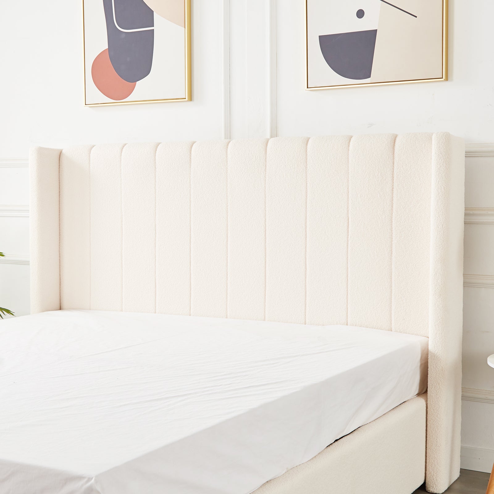 Septima & Fulvia Bouclé King Bed Base & Winged Headboard in Cream White, featuring a tall, tufted headboard and luxurious bouclé upholstery, with abstract art above and a hint of greenery beside.