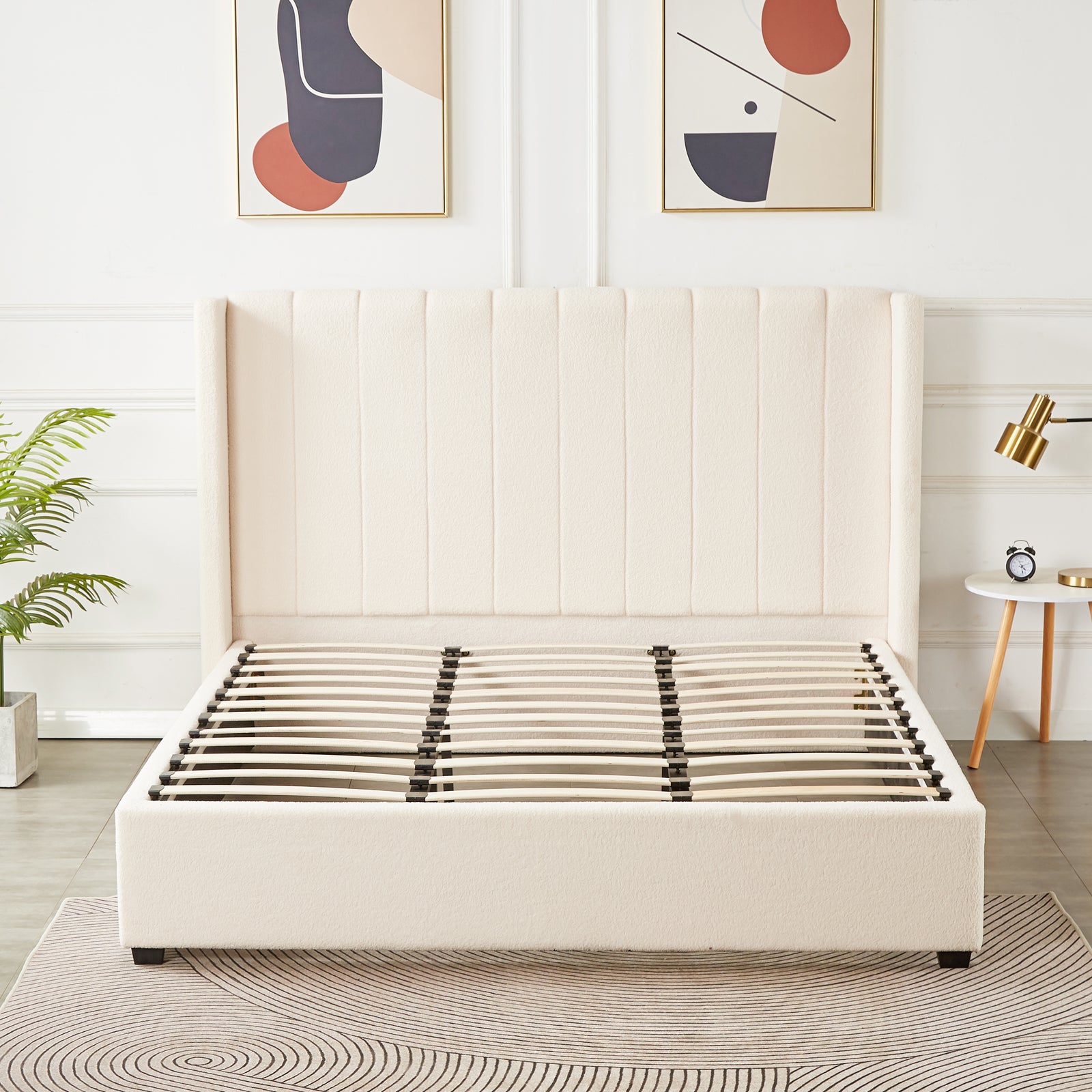 Septima & Fulvia Bouclé King Bed Base & Winged Headboard in Cream White features a tall, vertically-channeled headboard, exposed wooden slats, and complements minimalist decor with gold-framed art and a brass lamp.