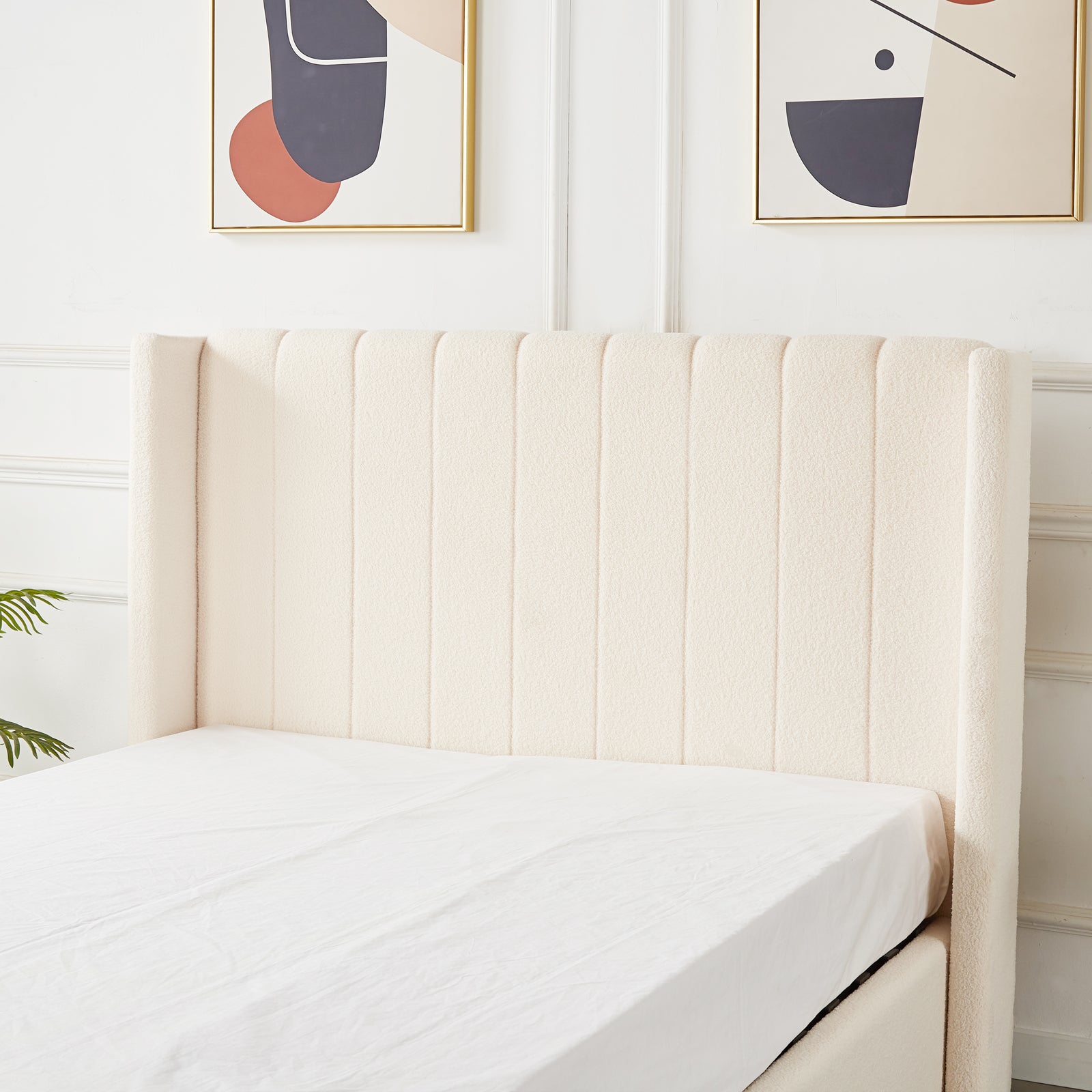 Septima & Fulvia Bouclé Queen Bed Base & Headboard in Cream White featuring a channel-tufted design, framed by abstract prints and a leafy plant, epitomizes modern elegance and minimalism in a bedroom setting.