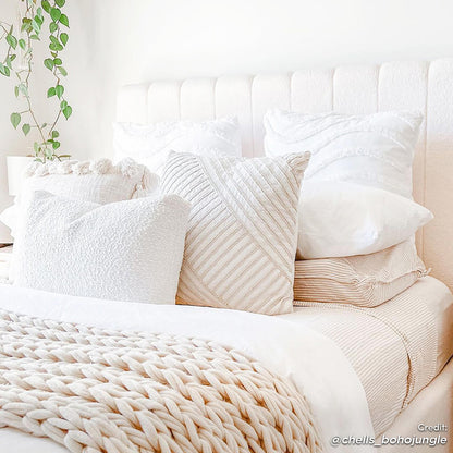 Septima & Gratiana Queen Bed Base & Headboard in Cream White, featuring a plush bouclé headboard with decorative pillows and a braided-knit throw, set against a neutral bedroom backdrop with a green houseplant accent.