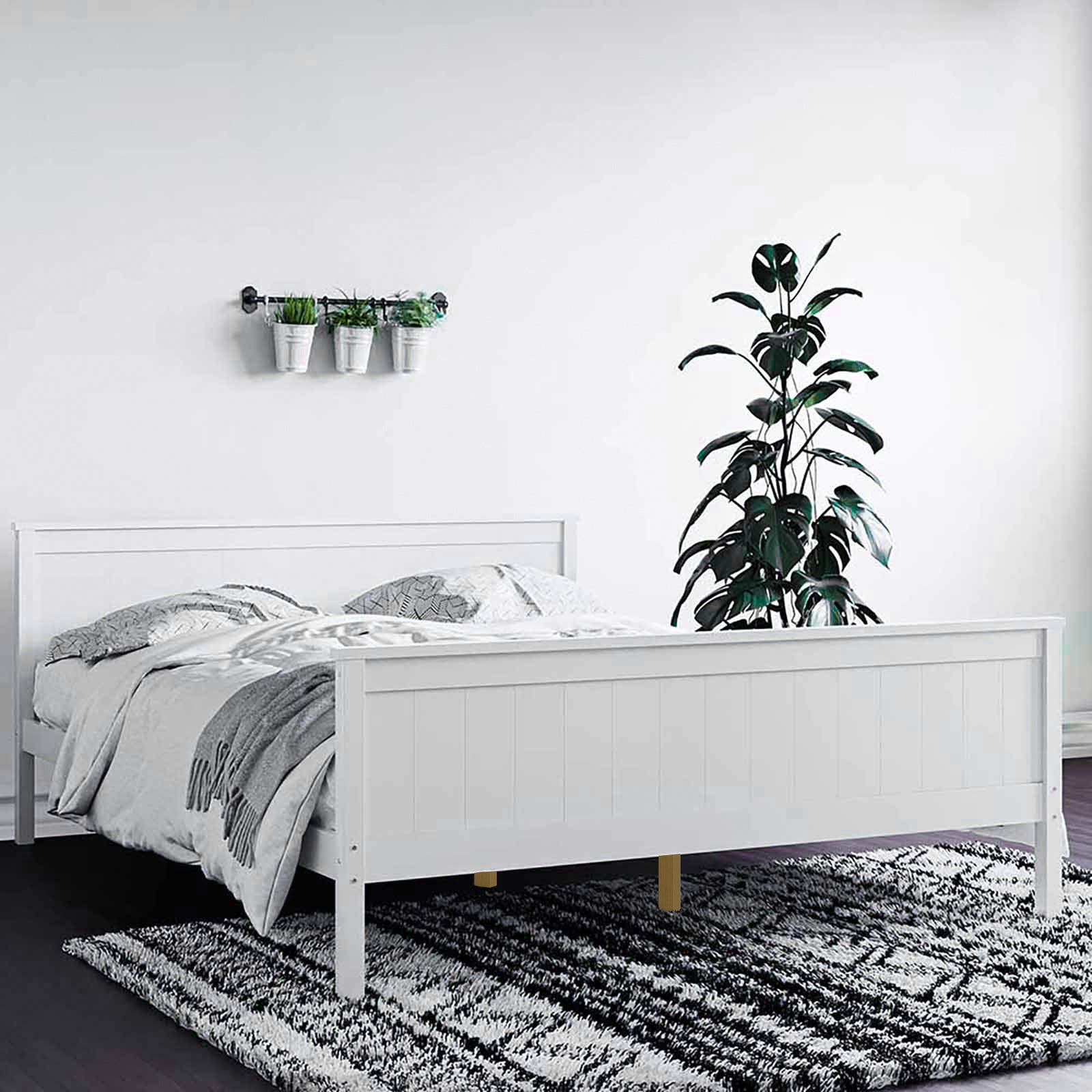 Close-up of the Tertia Solid Pine Timber Bed Frame Queen, showcasing its sturdy construction and elegant design, complemented by a black and white carpet underneath and a potted plant nearby.