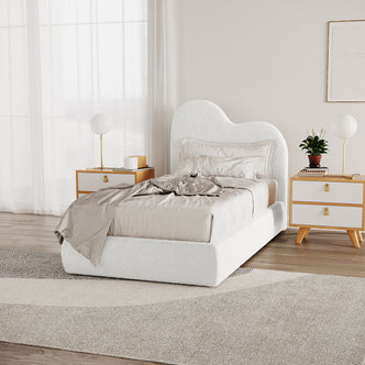 Thales Single Curved Boucle Fabric Bed Frame in Cream White, showcasing a cloud-like headboard. Features neutral silky bedding, mid-century nightstands, brass lamps, and a textured area rug in a minimalist bedroom setting.