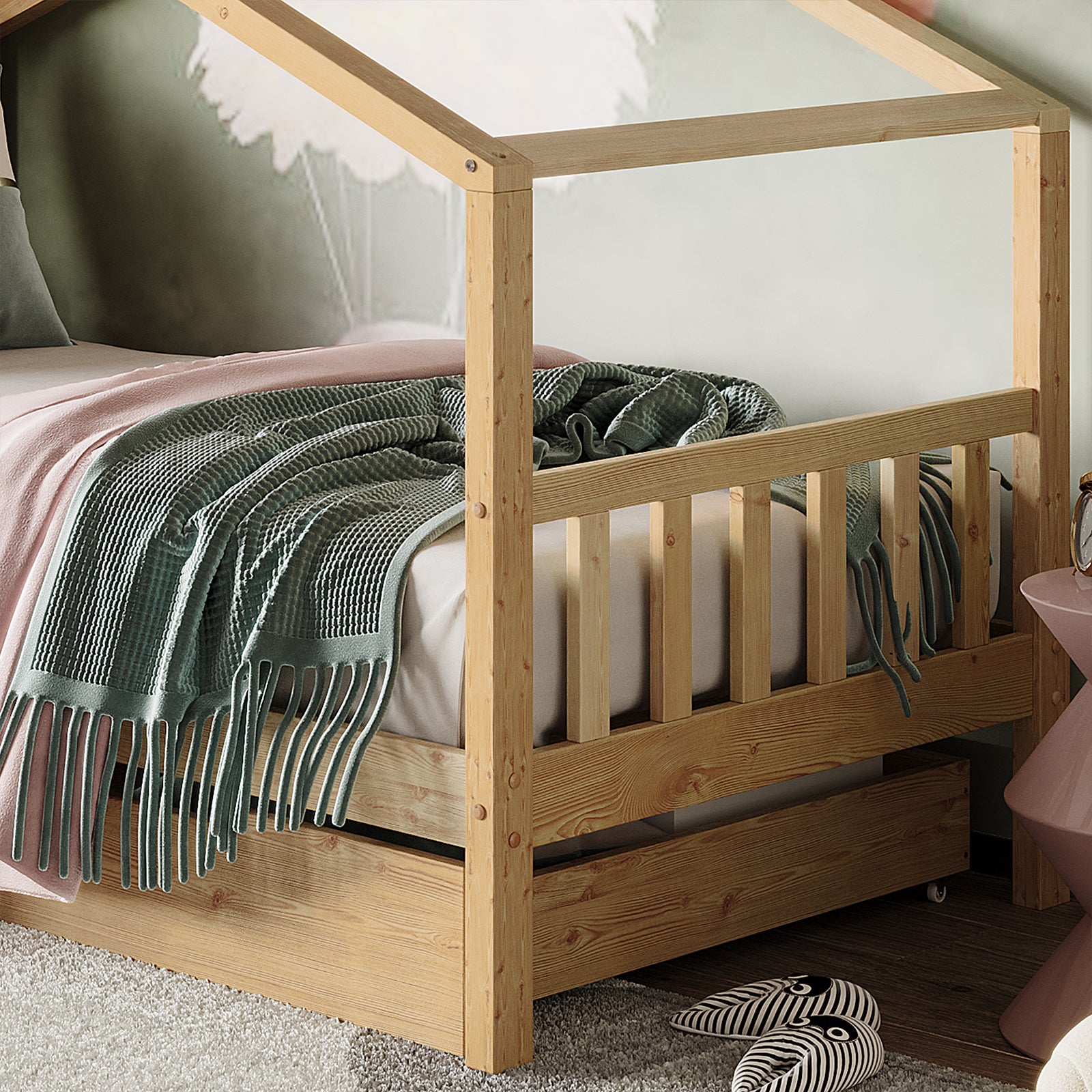 Tucker Solid Pine Timber Kids Bed with Drawers Natural featuring a house-frame design, slatted guardrails, pull-out storage drawer, pink bedside table, and striped slippers on a gray rug.