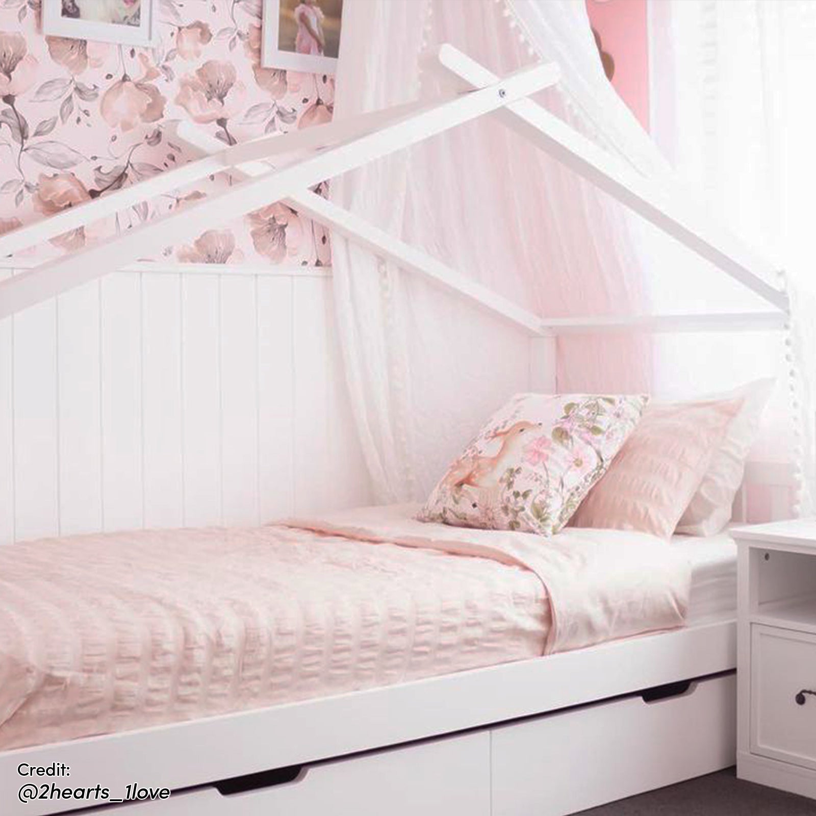 Tucker Solid Pine Timber Kids Bed with Drawers White features a house-shaped frame, soft pink bedding, tulle canopy, and two under-bed drawers in a pastel-pink children's bedroom setting.