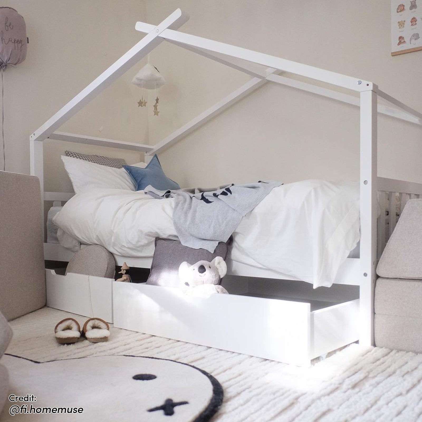 Tucker Solid Pine Timber Kids Bed with Drawers White features a house-frame design, white bedding, a pull-out drawer with a stuffed koala, and a cloud mobile, creating a cozy, imaginative space.