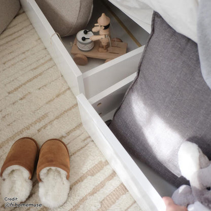 Tucker Solid Pine Timber Kids Bed with Drawers features two open storage drawers. A toy soldier and cushion with a plush elephant are visible, with brown slippers on a striped rug below.
